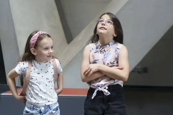 stock image Two cute beautiful schoolgirls look up with surprise and interest in the museum. Children's education concept