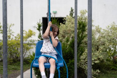 A little girl pulls a rope trying to lift herself in a chair. Concept of experimental children's education. clipart