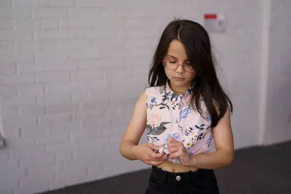 stock image A small beautiful sad girl in glasses looks down against the background of a brick wall. Child loneliness concept