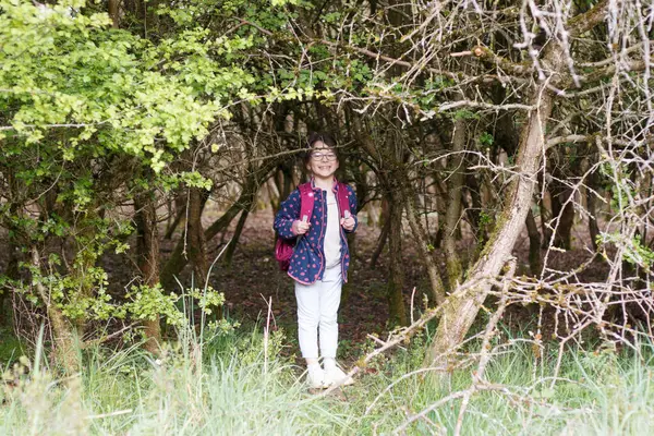 stock image Little girl with glasses and a backpack in the forest. Little traveler on a hike. Concept of children's wanderings