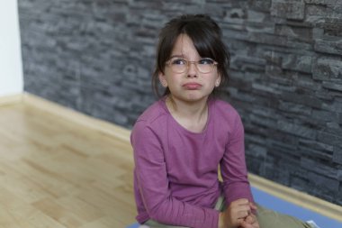 Little offended girl with glasses cries sitting on the floor. Concept of difficult child life clipart