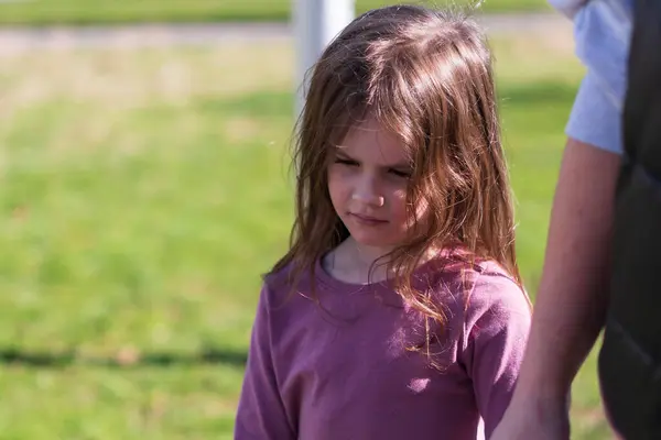 stock image A little cute red-haired girl holds her mother's hand while standing against a background of green grass. Family relationships concept