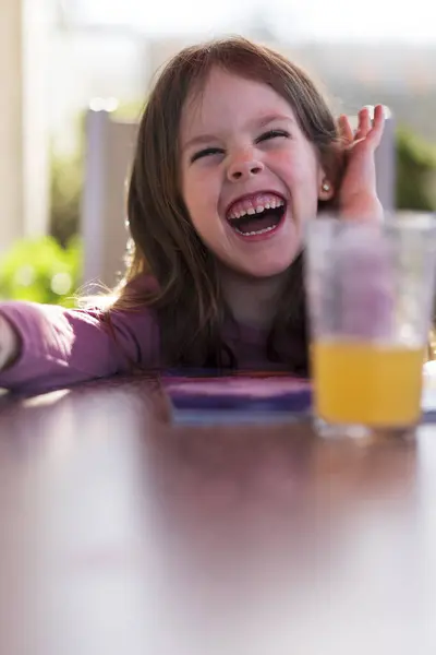 Stock image A cute little girl is reading a book while sitting at a table in the backyard on the terrace. Educational home concept