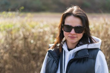 Güneş gözlüklü, gülümseyen siyah saçlı bir kız parkta uzun kamışların arkasında duruyor. İnsan ve doğa arasındaki birlik kavramı.