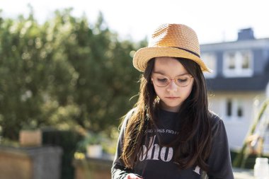 Hasır şapkalı küçük bir kız evinin terasında arka bahçede oturuyor. Mutlu çocukluk kavramı