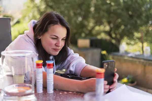 stock image A smiling cute girl takes a photo on her smartphone while reading on the terrace in the backyard of her house in the summer. Family happiness concept