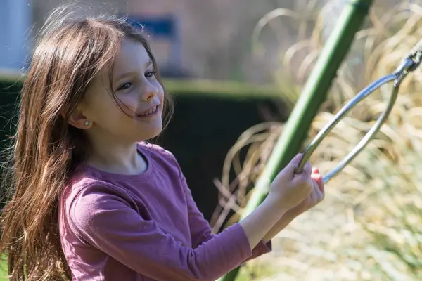 stock image A little girl swings from hanging rings in her backyard. Happy children's life concept