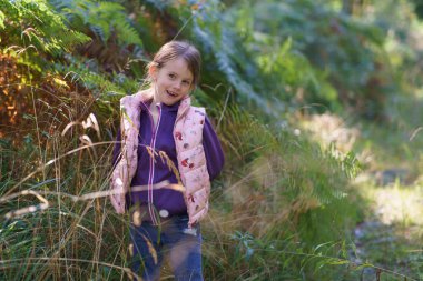 Karanlık bir sonbahar ormanının arka planında kapüşonlu ve yelekli güzel bir kız. Doğada mutlu bir çocukluk kavramı