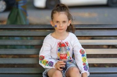 Iserlohn, NRW, Germany. August 24, 2024. Cute little girl in Ukrainian traditional embroidered shirt with Ukrainian flag on her cheek holding bottle of Coca Cola. Patriotic child concept clipart