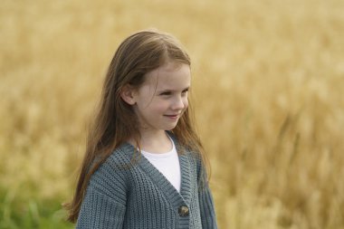 Tarlada olgunlaşmış buğdayın arka planında gülümseyen küçük tatlı kız. Çocukların eğlencesi, güvenliği, eğitimi, sağlığı, sigortası kavramı