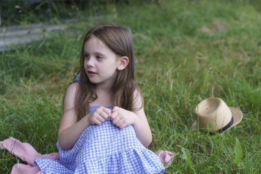 Çimlerin üzerinde küçük şirin bir kız ve hasır bir şapka oturuyor. Çocuk sağlığı, eğitim, eğlence kavramı