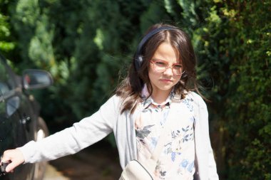 Büyük kulaklıklı, gözlüklü küçük bir kız yazın arabanın yanında durur ve kolu tutar. Çocukların seyahat, etkinlik, eğlence ve neşe kavramı