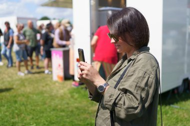 Koyu renk saçlı genç bir kadın yaz performansının arka planında cep telefonuyla fotoğraf çekiyor. Neşe, eğlence, seyahat ve duygu kavramı