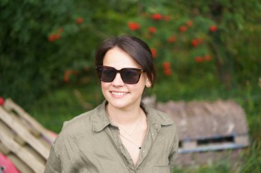 Güneş gözlüklü esmer kız ve yaz çiftliği geçmişinde poz veren yarım düğmesiz gömlek. Tarım, güzellik, bilgi ve seyahat kavramı