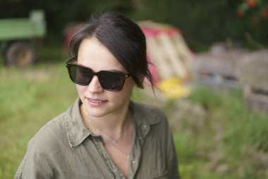 Güneş gözlüklü esmer kız ve yaz çiftliği geçmişinde poz veren yarım düğmesiz gömlek. Tarım, güzellik, bilgi ve seyahat kavramı