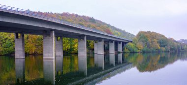 Almanya 'nın Iserlohn kentindeki Seilersee Gölü üzerindeki bir otoyol köprüsünün panoramik fotoğrafı. Arka planda sonbahar ağaçları.