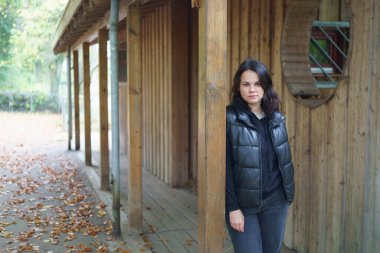 Koyu renk elbiseli güzel siyah saçlı kız sonbaharda ahşap bir kulübede poz veriyor. Dağ yolculuğu ve yürüyüş konsepti