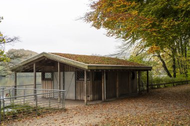 Sonbaharda bir gölün kıyısında küçük bir kulübe. Arka planda göletin üzerinde büyük bir köprü var.