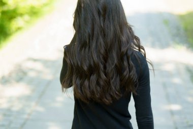 Uzun siyah kıvırcık saçlı güzel kız yaz parkında yolda yürüyor. Kameraya geri dönen ilginç bir çocuk.