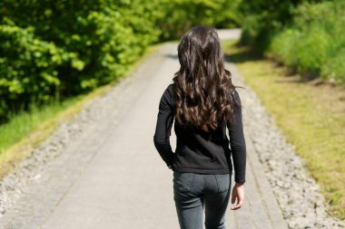 Uzun siyah kıvırcık saçlı güzel kız yaz parkında yolda yürüyor. Kameraya geri dönen ilginç bir çocuk.