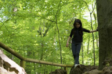 Active cheerful girl climbing rocks in summer forest. Concept of healthy active sporty child clipart