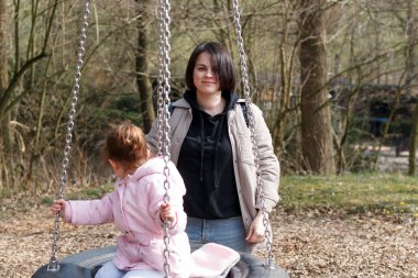 Mutlu genç anne bahar başında kızını salıncakta sallıyor. Aile eğlencesi kavramı.