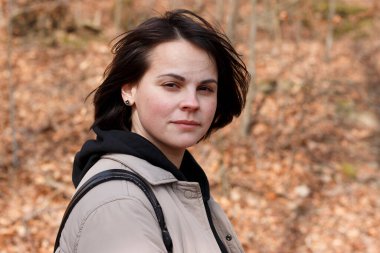 Koyu renk saçlı, gülümseyen bir kız ceketle açıkta yürüyor. Neşeli, aktif, sağlıklı bir kadın kavramı