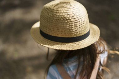 Sırt çantası ve hasır şapkalı küçük bir kız kameraya arkası dönük bir şekilde yaz parkında yürüyor. Çocukların yaz seyahati konsepti