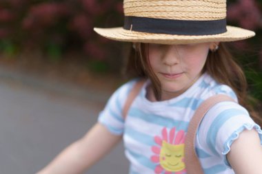 Sırt çantalı saman şallı küçük tatlı kız yazın seyahat ediyor. Bir çocuğun neşeli, aktif, sağlıklı çocuğu kavramı