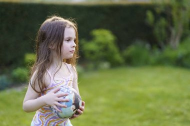 Little sad lightly dressed wet girl playing with ball in backyard in summer. Concept of cheerful active child clipart