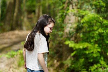 Gözlüklü ve tişörtlü küçük bir kız. Yazın ormanda ağacın yanında. Açık havada. Mutlu, aktif, sağlıklı çocuğun fotoğrafı.