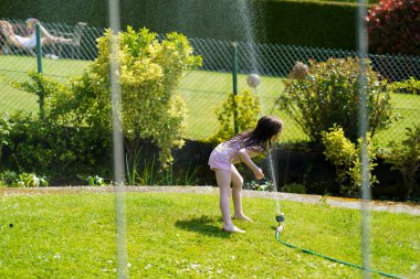 Little wet girl smiling playing with water sprinkler in summer in her backyard. Concept of children's fun healthy cheerful child clipart