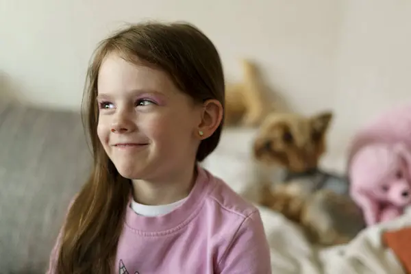 Göz makyajlı, pembe kazaklı, gülümseyen güzel bir kız kanepeye oturur ve arka planı bulanıktır. Sağlıklı neşeli aktif çocuk konsepti