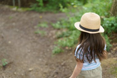 Yazın ormanda yürüyen hasır şapkalı küçük bir kız. Neşeli, sağlıklı bir çocuk kavramı