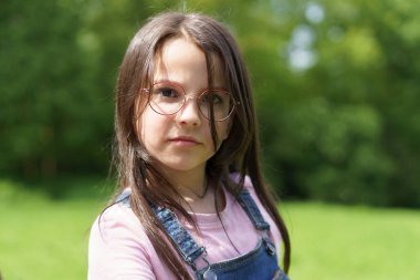 Gözlüklü ve kot pantolonlu küçük kız yazın dışarıda, parkta. Doğada aktif sağlıklı çocuk kavramı