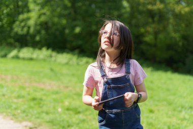 Gözlüklü ve kot pantolonlu küçük kız yazın dışarıda, parkta. Doğada aktif sağlıklı çocuk kavramı