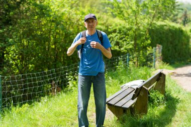 Senior man walking in a park with a backpack. Active backpacking travel concept clipart