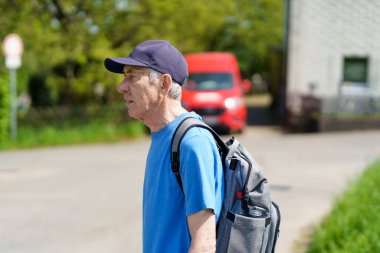 Omzunda sırt çantası olan yaşlı bir adam caddede yürüyor. Etkin seyahat konsepti