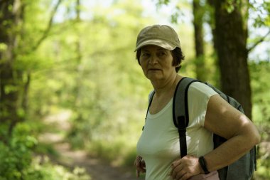 Ormanda yürüyüş yapan yaşlı bir kadın. Açık havada yürüyen aktif kıdemli bir kadın. Etkin seyahat konsepti
