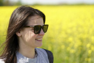 Güneş gözlüklü genç bir kadın çiçek açan bir ırz tohumu tarlasında. Etkin seyahat konsepti