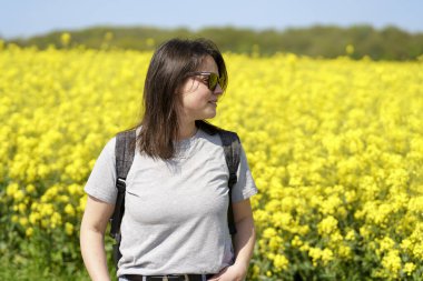 Çiçek açan bir kolza tohumu tarlasının ortasında genç bir kadın. Etkin seyahat konsepti