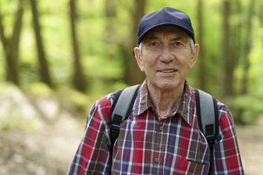 Ekose gömlekli ve şapkalı yaşlı bir adam ormanda dikiliyor. Yaşlılıkta aktif seyahat kavramı