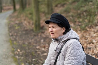 Ceketli ve şapkalı yaşlı bir kadın parkta bir bankta tek başına oturuyor. Yaşlılıkta yalnızlık kavramı.