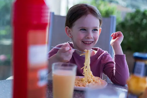 Küçük tatlı kız dışarıda soğuk bir içecekle yaz masasında oturmuş makarna yiyor. Sağlıklı çocukluk beslenme kavramı