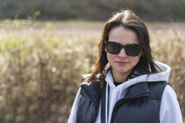 Baharda dışarıda dikilen güneş gözlüklü ve yelekli tatlı, güler yüzlü kız. Sağlıklı aktif kişi kavramı