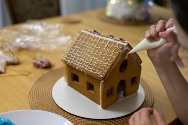 Küçük çocukların elleri kurabiyelerden yapılmış bir Noel evini süslüyor. Çocukların yaratıcılık kavramı