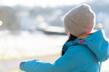 Sad teenage girl in glasses, hat and winter jacket on the street, side view. Concept of difficult childhood clipart