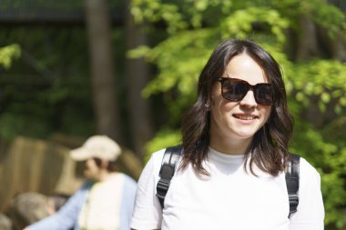 Sırt çantalı, beyaz tişörtlü, yaz parkında oturan güzel bir kız. Aktif yürüyüş konsepti