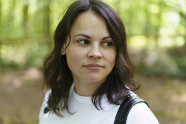 Sırt çantalı, beyaz tişörtlü, yaz parkında oturan güzel bir kız. Aktif yürüyüş konsepti