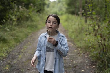 Gözlüklü küçük tatlı kız yaz ormanlarında elinde bitki üflüyor. Çocuklar yürüyüş ve eğlence konsepti